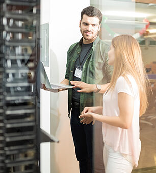 Two business people standing in server room with laptop and discussing